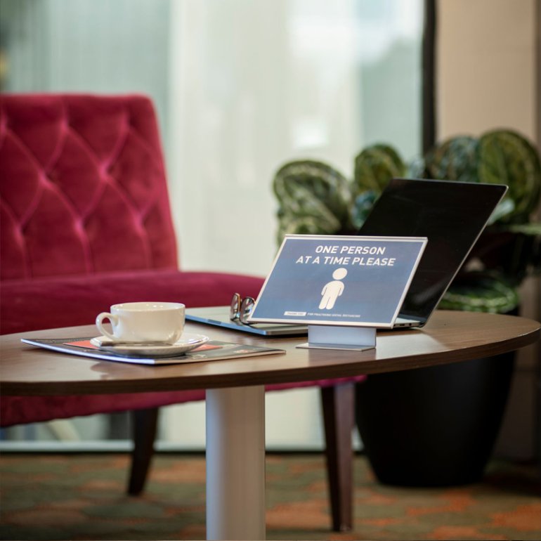 Absolute Freestanding Label holder placed on a table in an office environment informing social distancing measures.